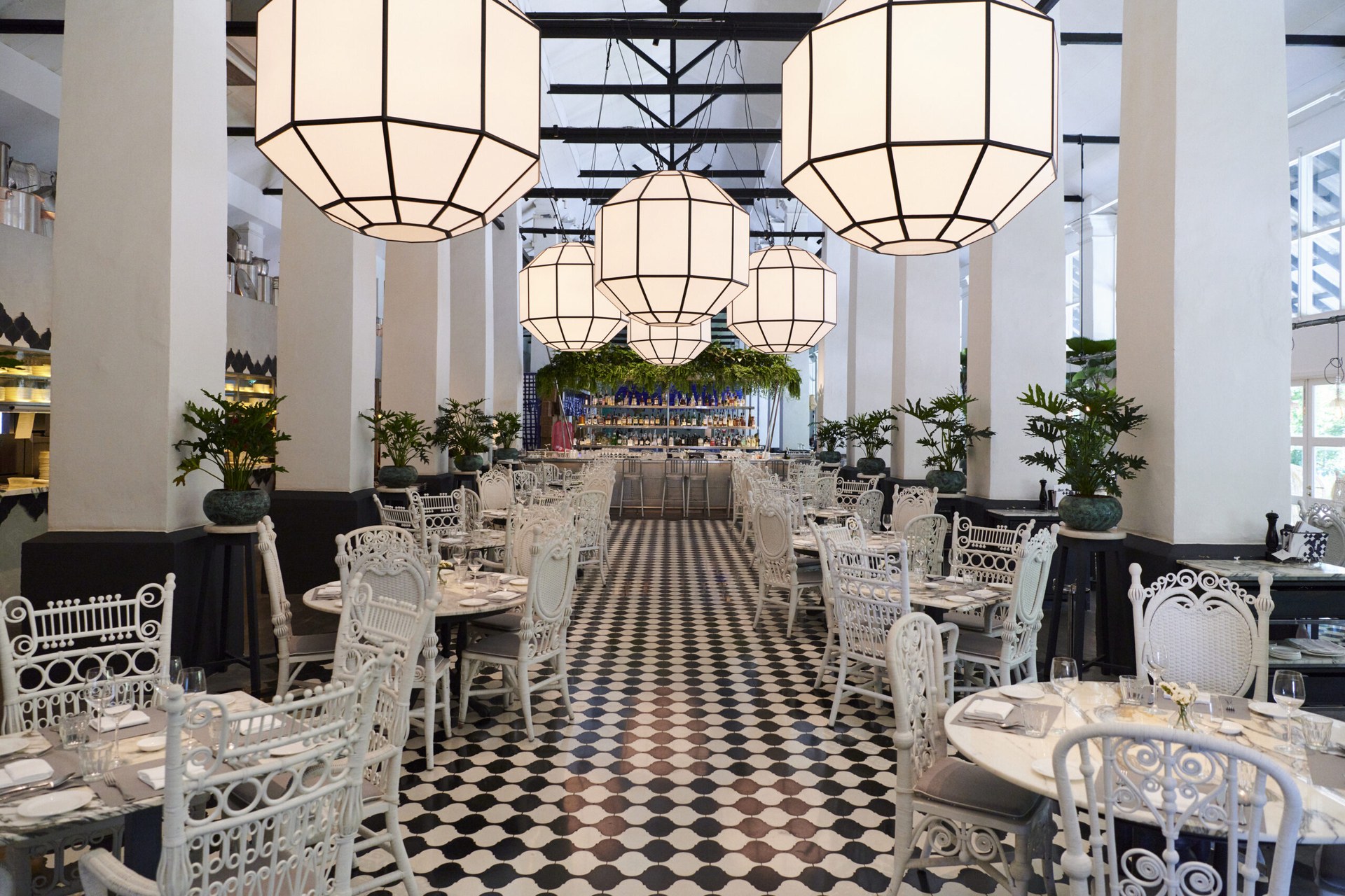 A dining room at COMO Dempsey, with white lanterns, wrought-iron chairs and a chequered floor